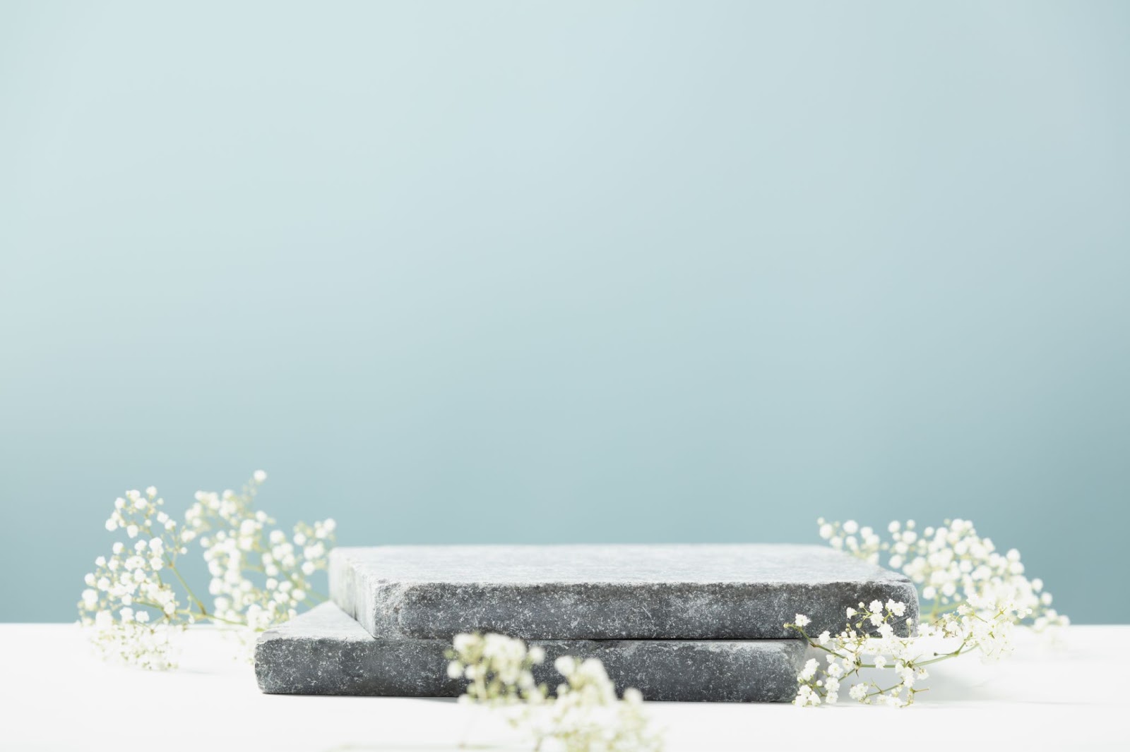 Flat granite pedestal and white flowers on blue background