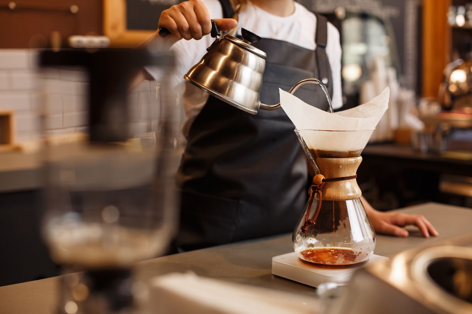 A lifestyle photography shot of a professional barista preparing coffee using chemex pour over coffee maker and drip kettle