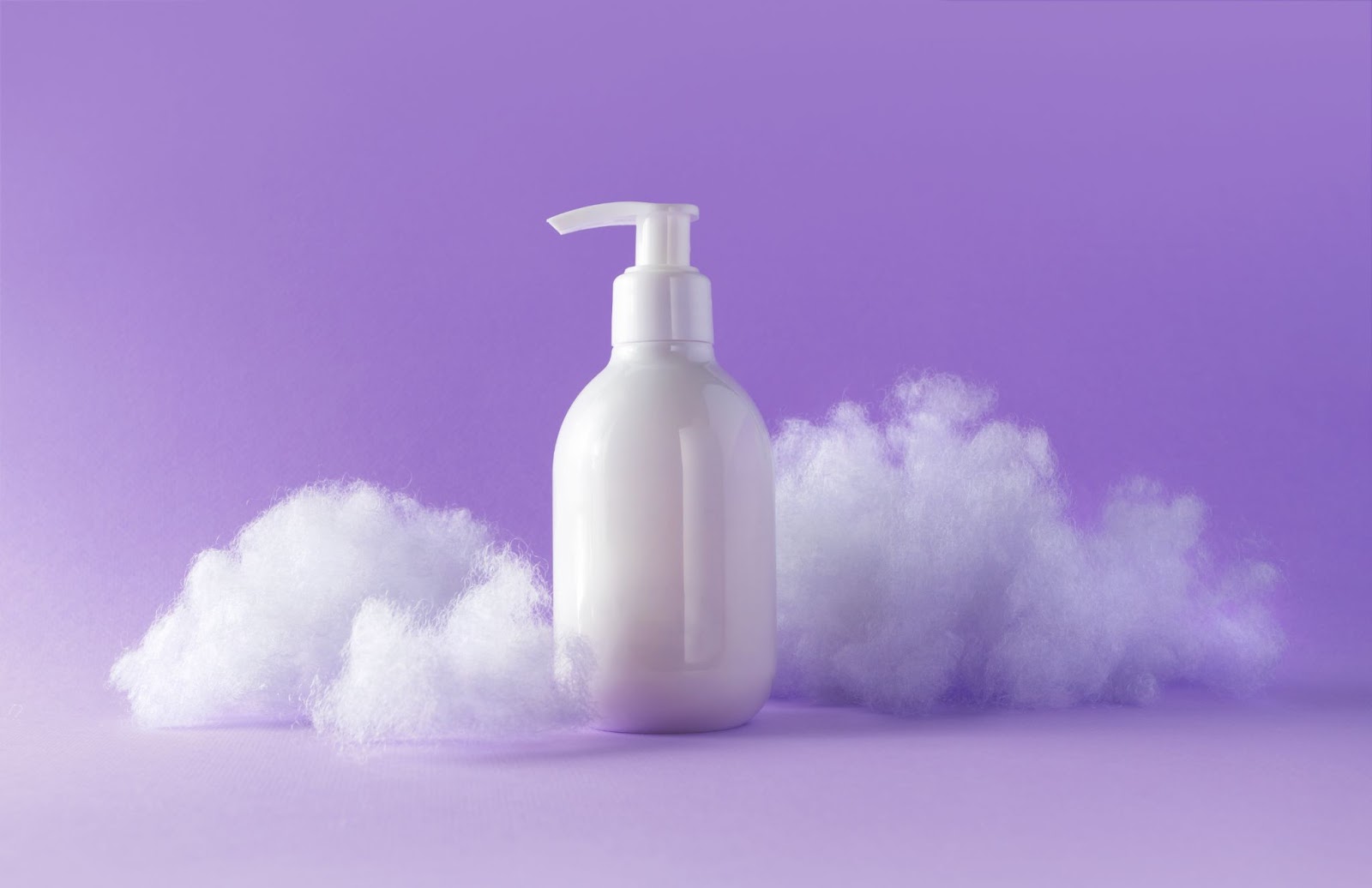 A bottle of lotion with fluffy clouds on violet background