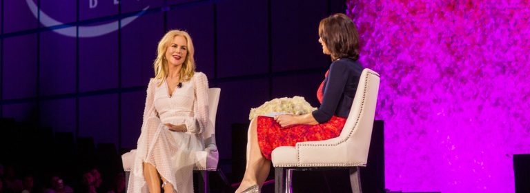 Nicole Kidman speaking on stage at a Houston event, one with blonde hair and the other with dark hair.