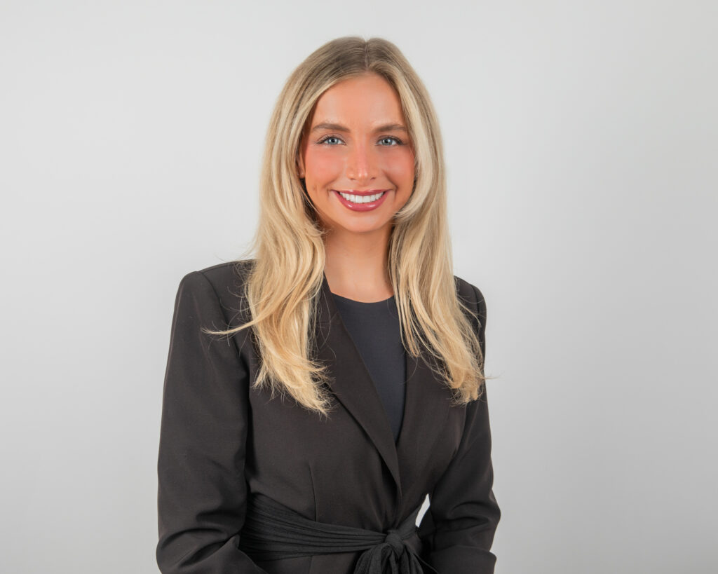 A blond woman in a black blazer smiles for a professional corporate headshot.