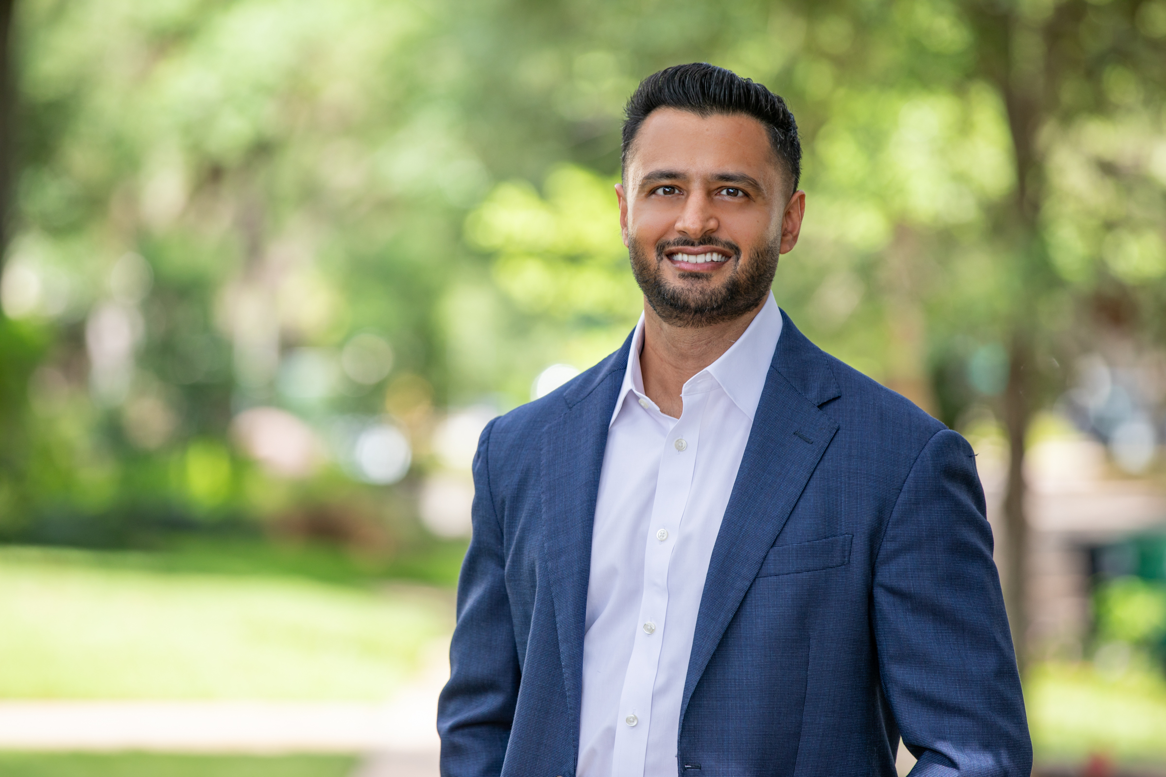 Outdoor professional headshot of a man with an open collar and blue suit jacket.