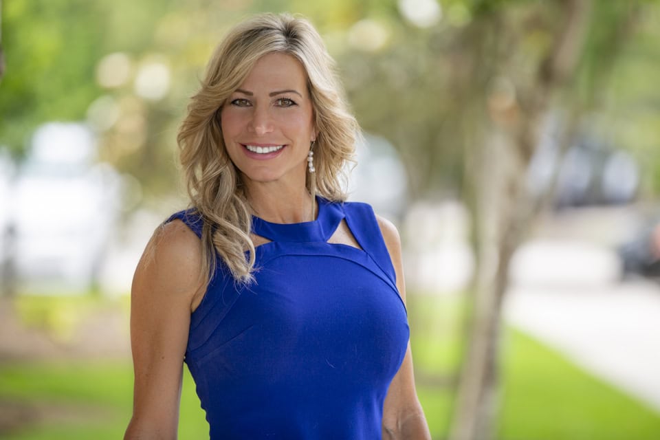 Headshot of smiling woman in blue dress outdoors for professional profile.