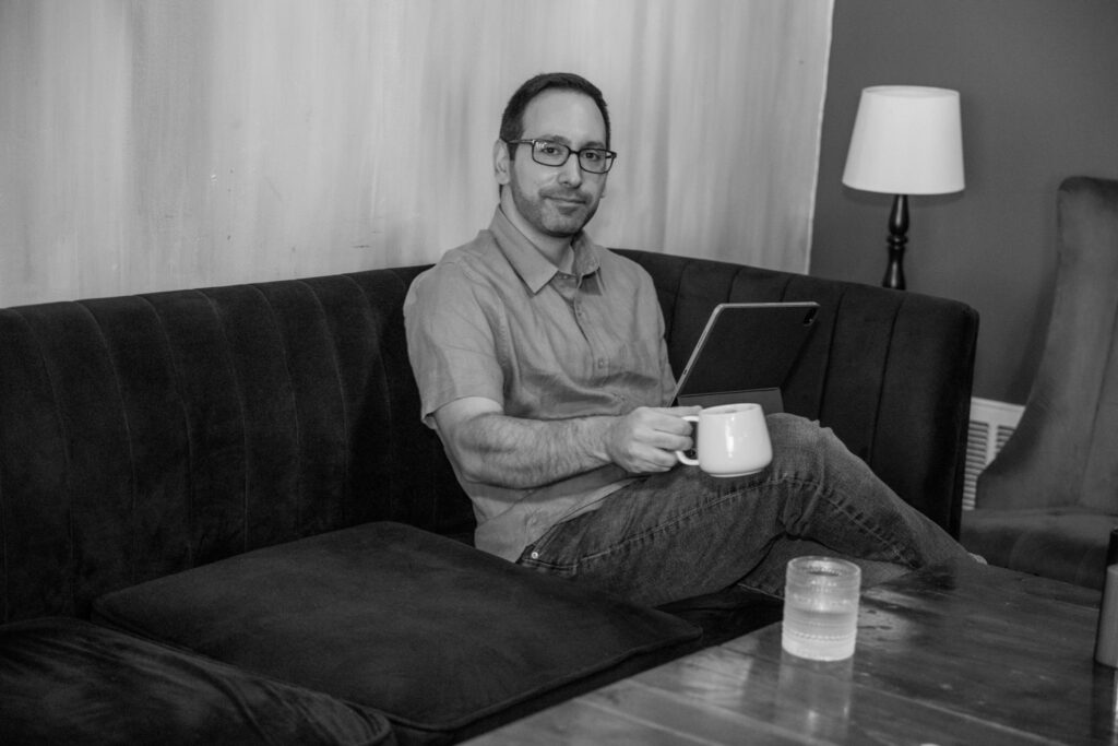 man sitting on a couch holding a coffee mug and tablet in a cozy lounge setting