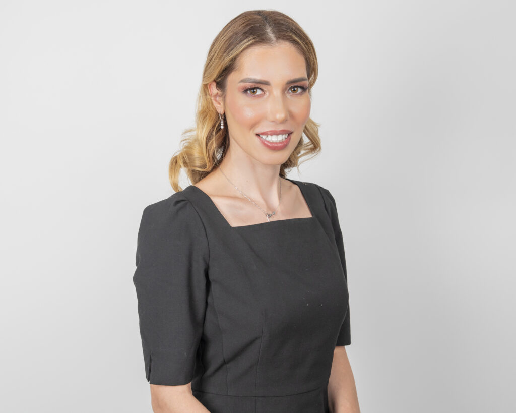 Studio portrait of a woman smiling in professional attire, photographed against a light background.