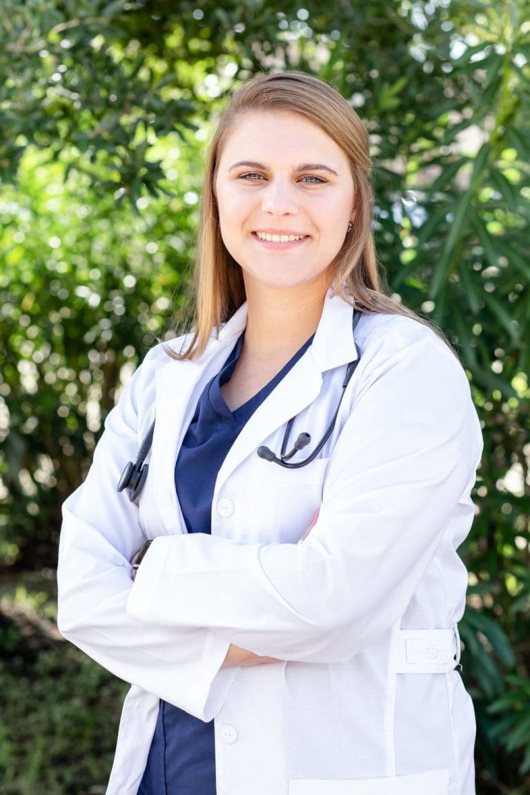 Smiling female healthcare professional in white coat outdoors.