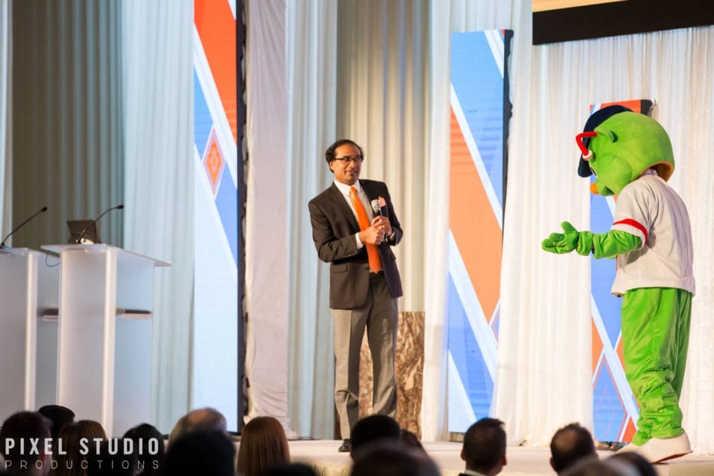 Business speaker on stage with mascot at conference event.