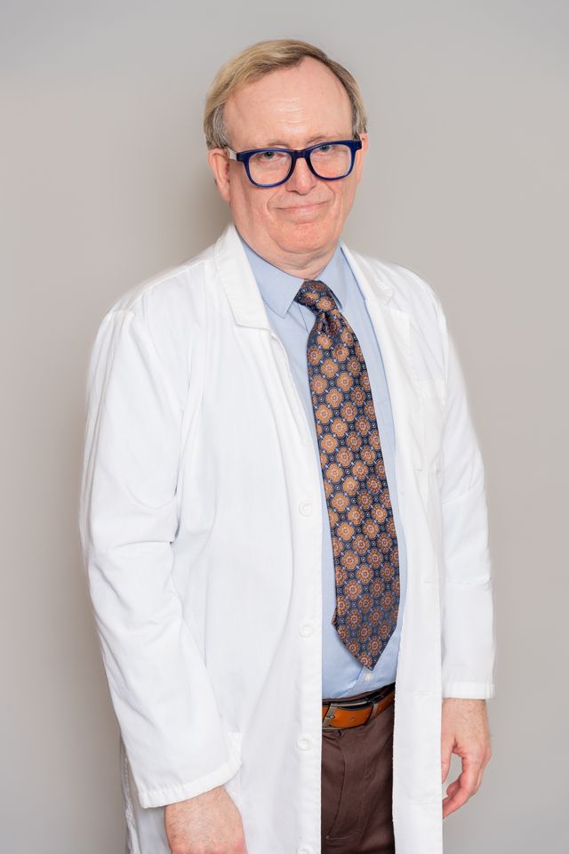 Senior male physician in a white coat and glasses, professional studio portrait by Pixel Studio Productions