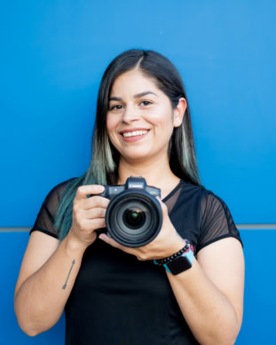 Vessy, Pixel Studio Productions photographer, holding a Canon camera against a blue wall