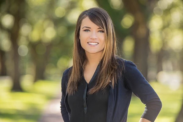 Young woman smiling outdoors, professional headshot for business or LinkedIn profile.