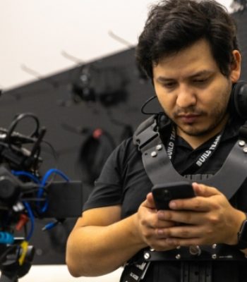 Alex, Pixel Studio Productions videographer, on set wearing a camera rig and checking his phone