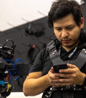 Alex, Pixel Studio Productions videographer, on set wearing a camera rig and checking his phone