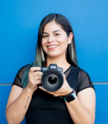 Vessy, Pixel Studio Productions photographer, holding a Canon camera against a blue wall