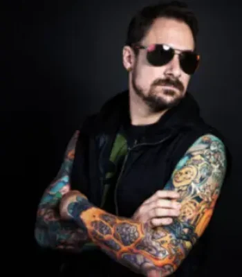 Slade, Pixel Studio Productions animator, studio portrait in sunglasses with tattooed arms crossed