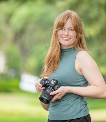 Pixel Studio Productions photographer holding a camera, outdoor portrait in a teal top